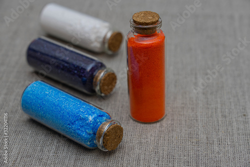 Blue, red, white and indigo powder and crystalls crystals in small bottles on gray linen background