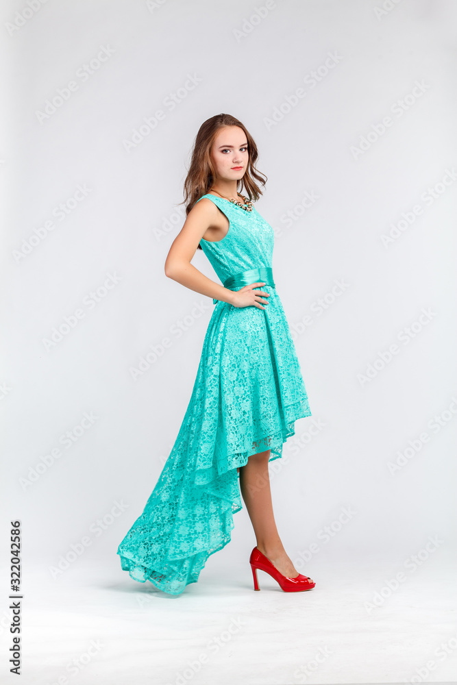 Beautiful young girl in long evening turquoise dress, goes in full length, motion, gait, guipure dress with plume, isolated on white background. Looks at the camera. Photo from the series Beautiful young girl in long evening turquoise dress, goes in full length, motion, gait, guipure dress with plume, isolated on white background. Looks at the camera. Photo from the series