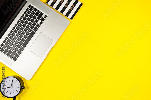Business concept of laptop, clock  and small notepad on bright yellow background with copy space, view from above, mock up photo