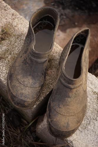 A pair of old dirty galoshes with water inside on stones.