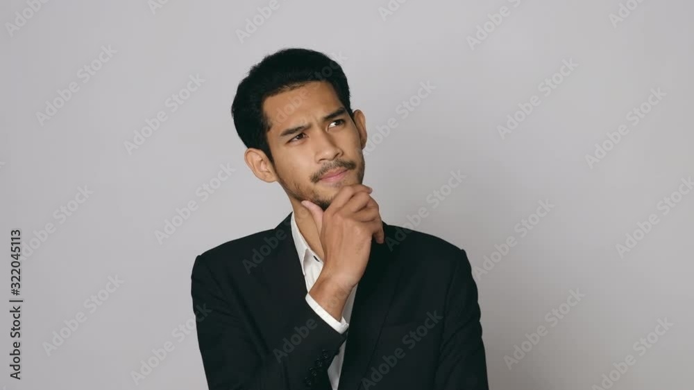 Thoughtful young asian businessman holding hand on chin over gray background, thinking and having idea. Thoughtful young asian businessman holding hand on chin over gray background, thinking and having idea.