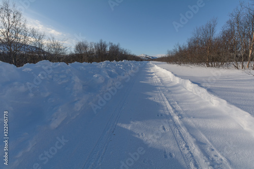 The dirt road is covered with ice and snow .Clear blue sky.