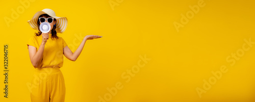 Cute and funny woman in yellow casual cloth style and wearing hat holding white megaphone for announcement and show hand to present product