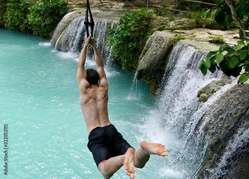 Man jumping from cliff into natural pool before waterfall , in air, cambugahay falls, Siquijor, Philippines