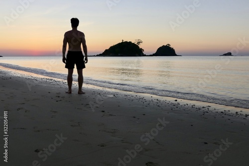 Man standing at Nacpan beach during sunset , before small island, El Nido, Palawan, Philippines photo