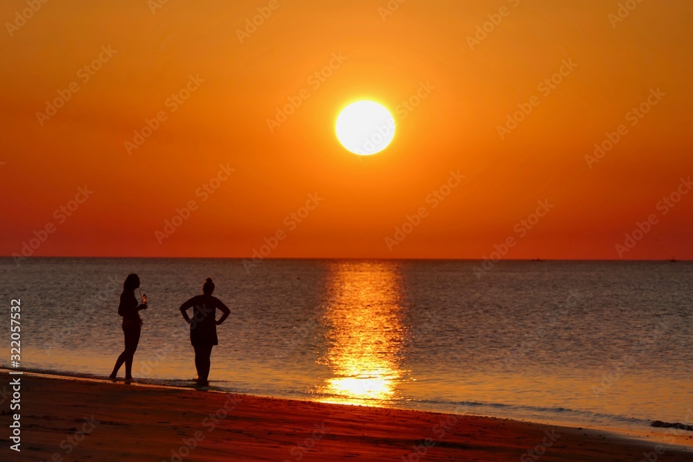 Sunset with orange sky at Nacpan beach with two girls, El Nido, Palawan, Philippines Sunset with orange sky at Nacpan beach with two girls, El Nido, Palawan, Philippines