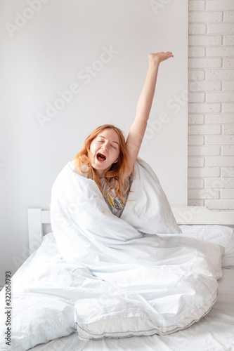 Blonde woman while stretching on bed after waking up with sunrise at morning. Vertical photo photo