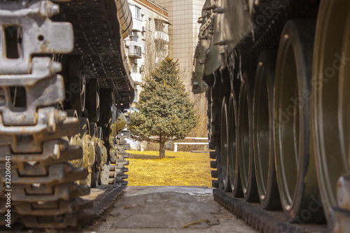 View of a young Christmas tree, spruce through the window between the tracks of two military tanks.