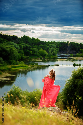Full length portrait of beautiful sensual young blond woman in long pink dress and floral wreath near the lake outdoors in natural background.