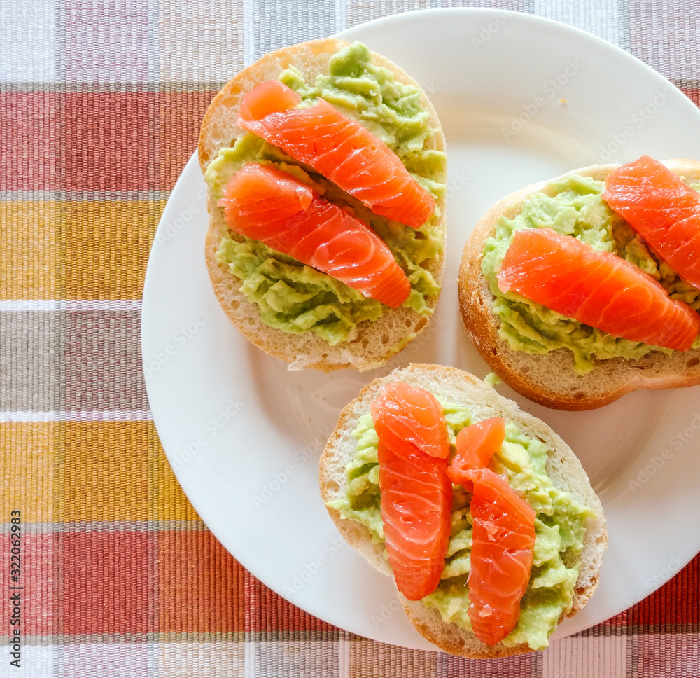 Bread with avocado and slices of smoked salmon on the plate and kitchen cloth, top view
