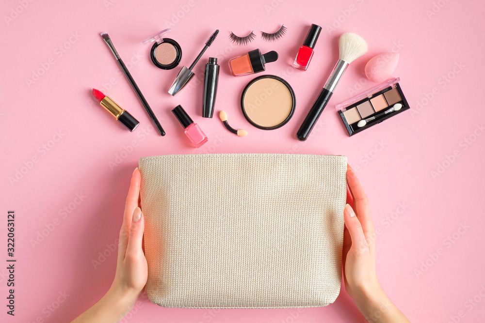 Female hands holding makeup bag with cosmetic beauty products over pink