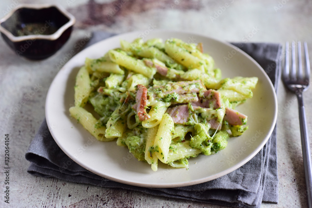 Italian pasta with ham and broccoli sauce, cheese and cream on a white plate close-up on a gray background Italian pasta with ham and broccoli sauce, cheese and cream on a white plate close-up on a gray background