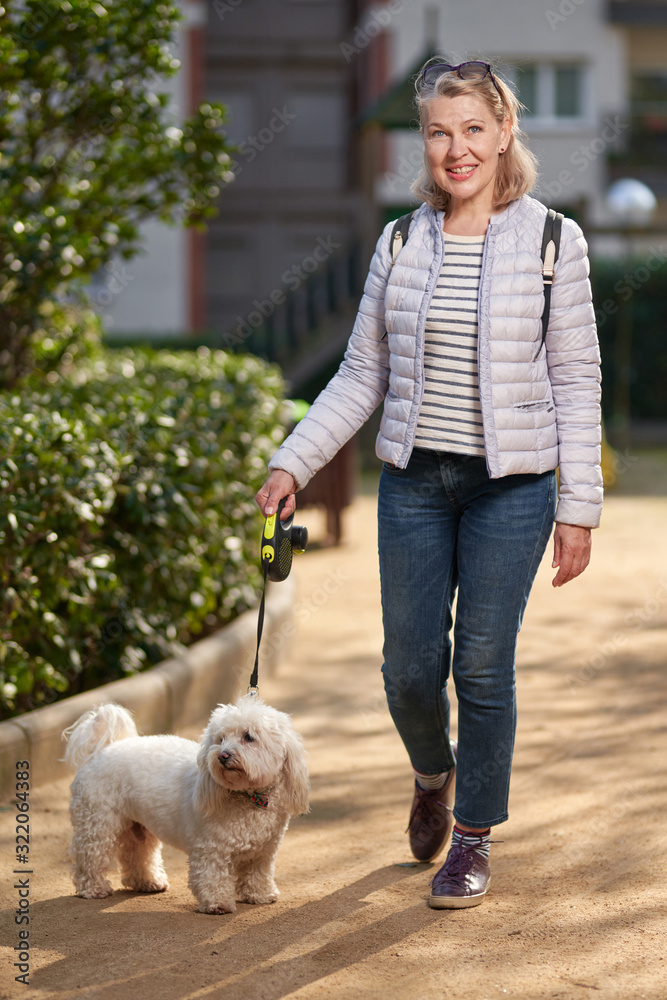 middle-aged woman walking with fluffy white dog in summer city middle-aged woman walking with fluffy white dog in summer city