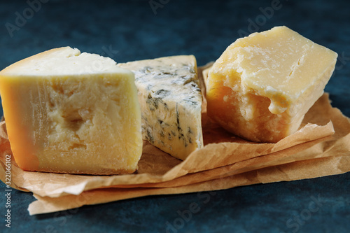 Different sorts of cheese on a parchment paper on dark blue textured background. ?lose up