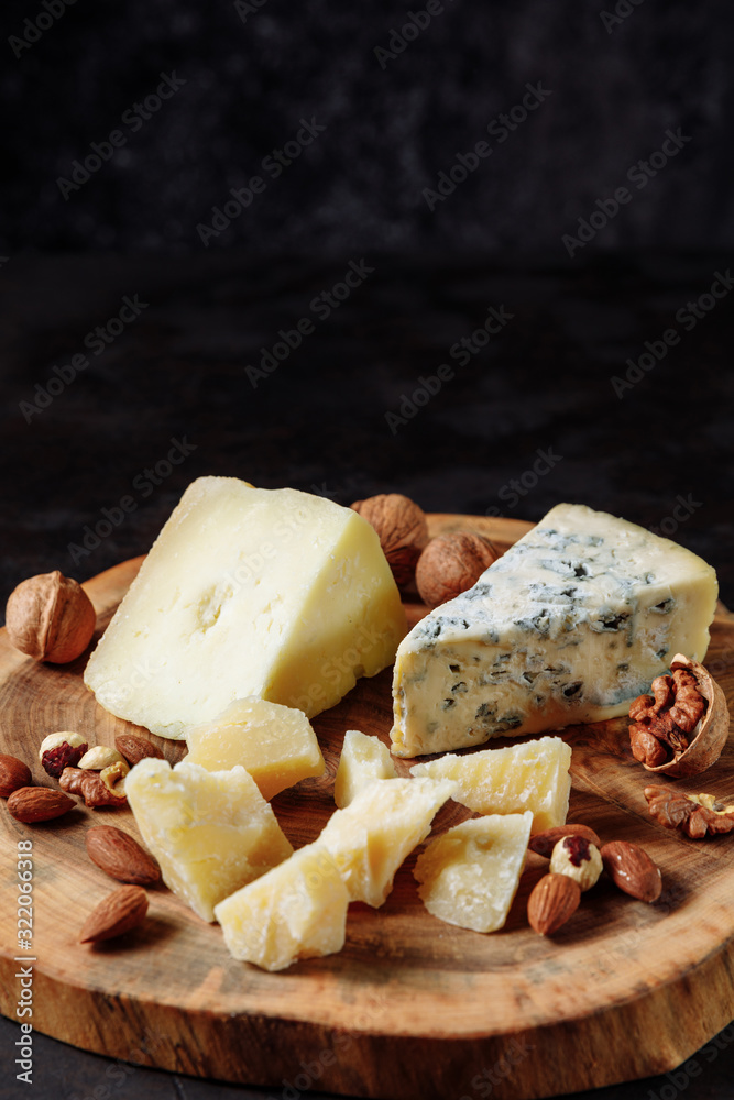 Tasting cheese plate with parmesan, dorblu, sheep milk cheese, almonds, nuts on a wooden saw cut board on a dark background. Appetizer, aperitif, snack table. Space for text