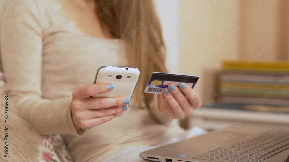 The Girl Pays for Online Purchases Using a Bank Credit Card Using a Smartphone Cell Phone Through a Mobile App on the Internet. Camera Slide. The Girl Pays for Online Purchases Using a Bank Credit Card Using a Smartphone Cell Phone Through a Mobile App on the Internet. Camera Slide.