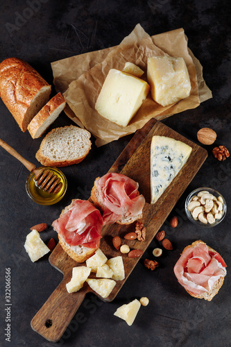 Tasting prosciutto and cheese platter with parmesan, dorblu, almonds, nuts, bread and honey on a wooden board on a dark background. Appetizer, aperitif, snack table. Top view