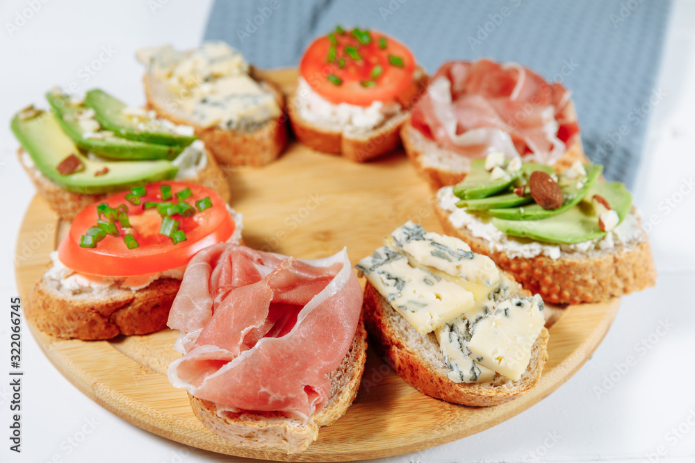 Traditional Italian bruschette snack on a wooden plate on a white wooden table and gray napkin. Mini sandwich mix Traditional Italian bruschette snack on a wooden plate on a white wooden table and gray napkin. Mini sandwich mix