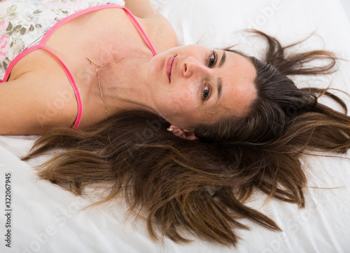 Top view of woman with flowing hair posing in bed in bedroom