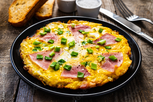 Breakfast - scrambled eggs with ham and vegetables on wooden background