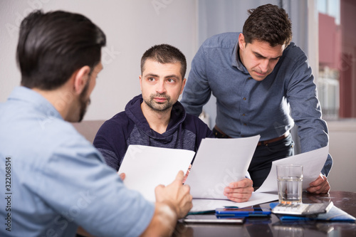 Three upset males with papers at table