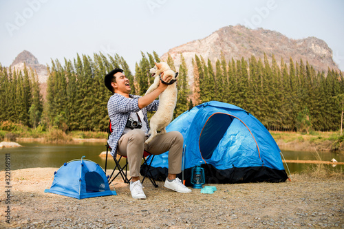 Asian young man in blue shirt with cute puppy dog camping on the lake hill mountain view happy and enjoy life