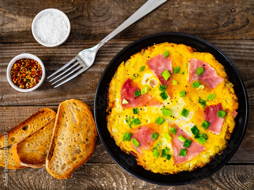 Breakfast - scrambled eggs with ham and vegetables on wooden background
