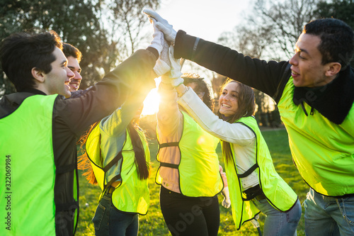 Teamwork - Business team success - Six people with yellow bibs beat high five in the air at the park at sunset after community service - Concept of unity and collaboration photo