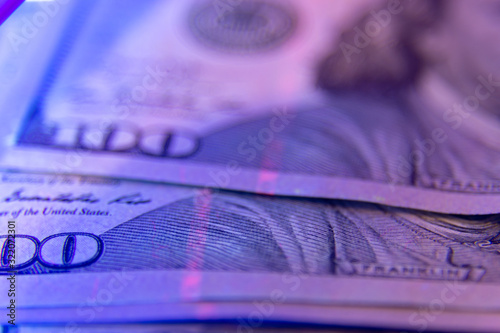 Soft focus on dollar banknote under ultraviolet light. Benjamin franklin portrait being inspected. Money falsification concept background.
