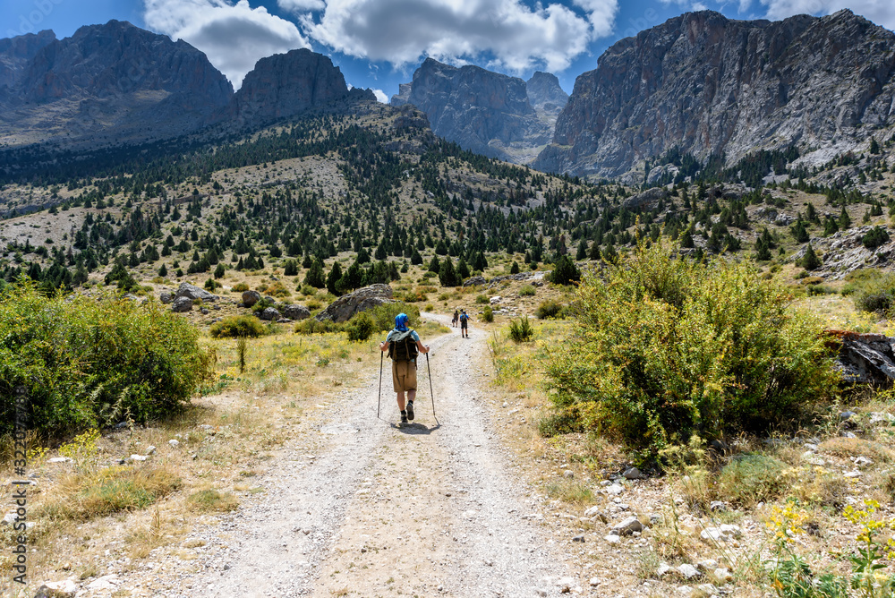 Turkey, Chamard - August 3, 2019: Tourists walk along the road through the mountain landscape in the Turkish national Park aladag in summer day, view from the back