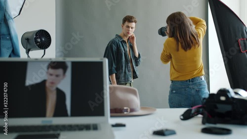 People model and photographer in studio during photoshoot working indoors, guy is posing while girl is taking pictures with modern camera. Youth and creativity concept. photo