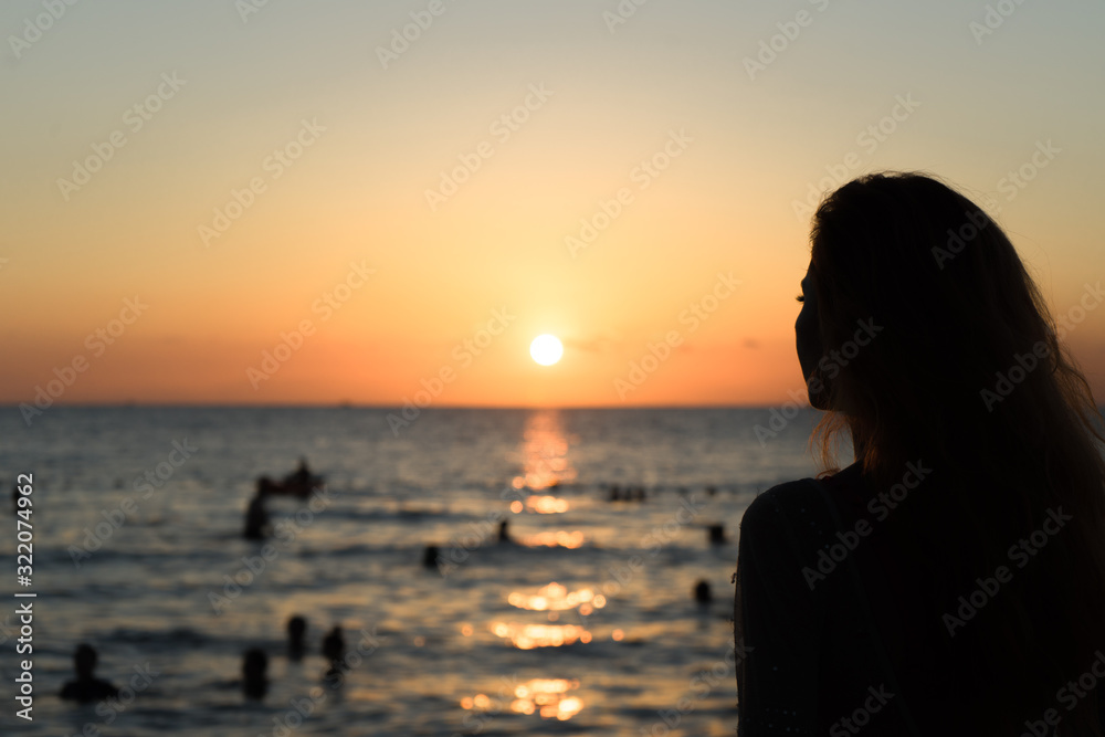 Girl on the beach looks at the sunset.