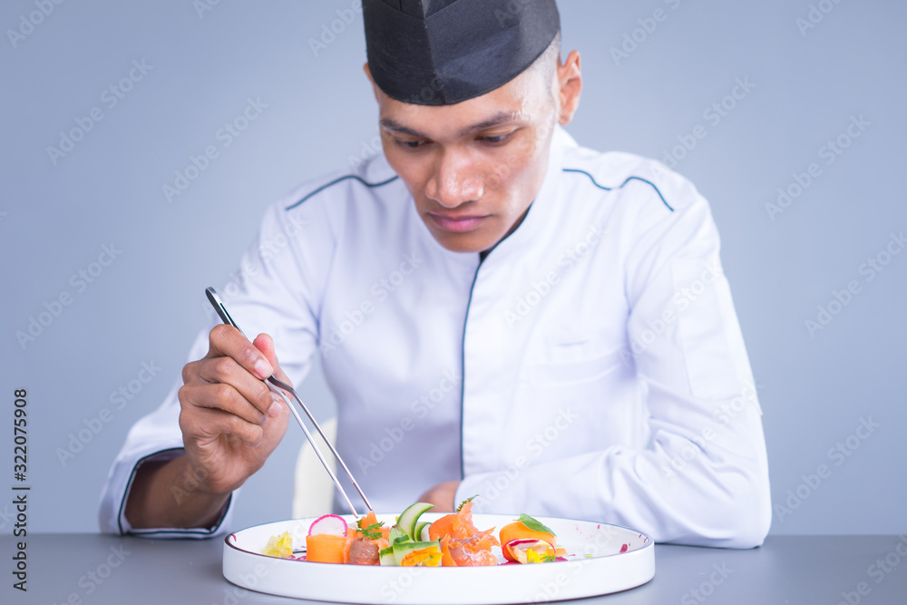 An Asian Executive Chef plating his dish carefully putting his finishing touch to the vibrant dish.