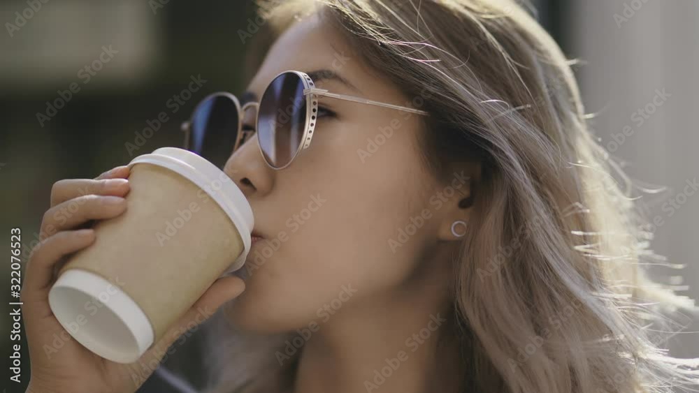 beautiful Asian blonde girl in sunglasses drinking coffee on the go, taste of fresh aromatic coffee, cheerful morning