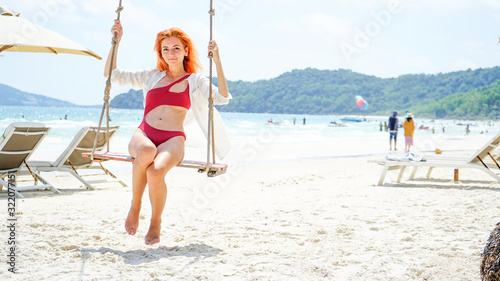 Long red haired woman sitting on the swing on the tropical Bai Sao beach on Phu Quoc island, Vietnam.