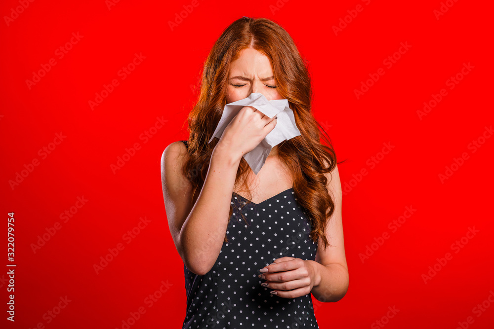Young girl sneezes into tissue. Isolated on red woman is sick, has stuffed or runny nose and fever. Coronavirus, epidemic 2020, illness concept.
