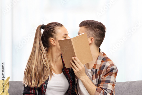 Young male and female kissing behind a book