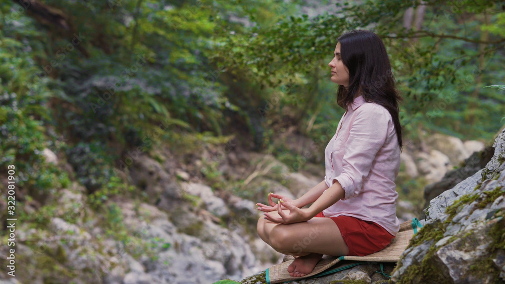 A woman with closed eyes in the Lotus position sits on a rock in the middle of the forest and meditates. A woman with closed eyes in the Lotus position sits on a rock in the middle of the forest and meditates.