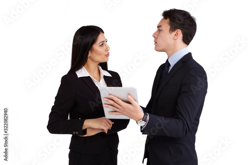 A young business man is reprimanding a young business woman. He is holding a tablet. He looks unhappy and intimidating. She is looking at him.