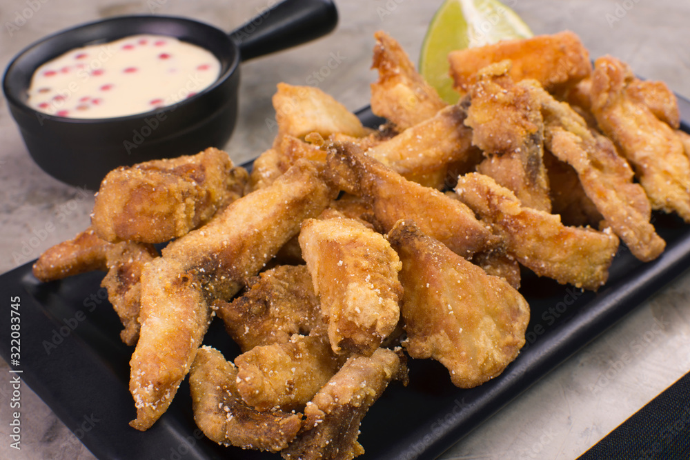 Fried Tilapia strips in a black platter close with rose pepper sauce in
