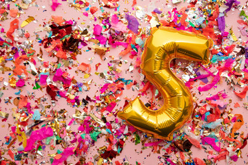 Number 5 gold birthday celebration balloon on a confetti glitter background