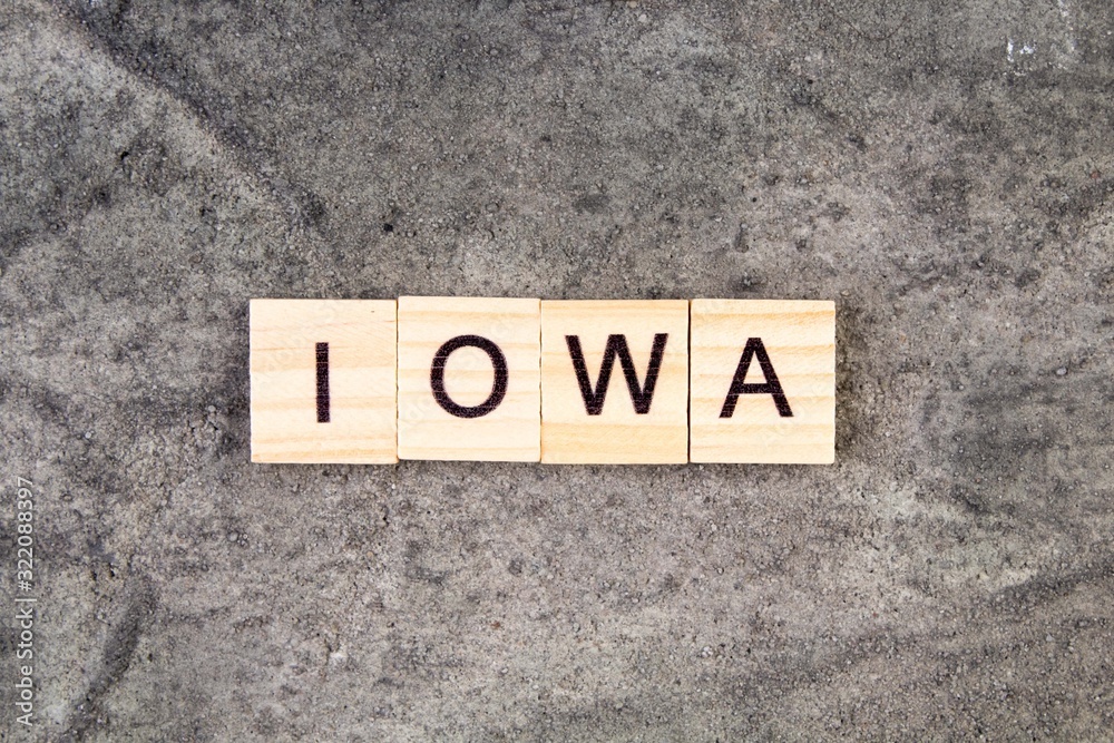 Iowa word written on wood block, on gray concrete background. Top view. Iowa word written on wood block, on gray concrete background. Top view.