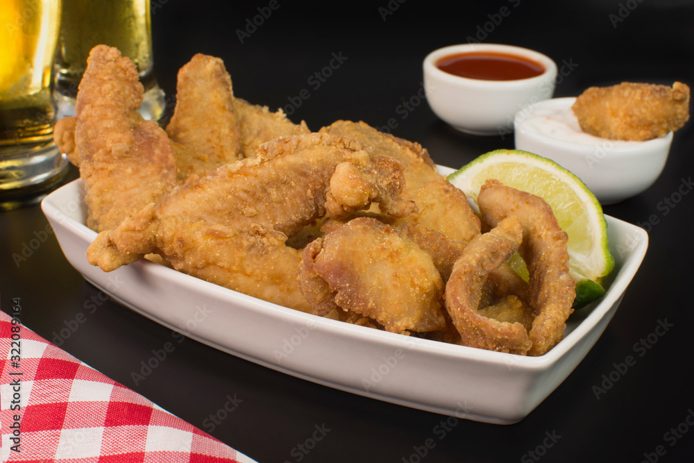 Fried Tilapia strips in platter with beer and sauces in black background Fried Tilapia strips in platter with beer and sauces in black background