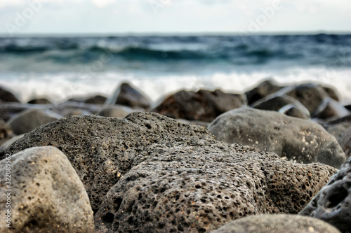 A large porous stone on the seashore. A rocky beach on which the wave rolls.