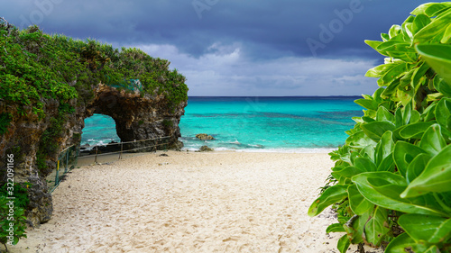 Travel to famous Paradise beach of Sunayama on Miyako Island in Japan. Seascape against blue stormy sky before rain, bright birch water, snow-white sand and a stone cliff overgrown with greenery 