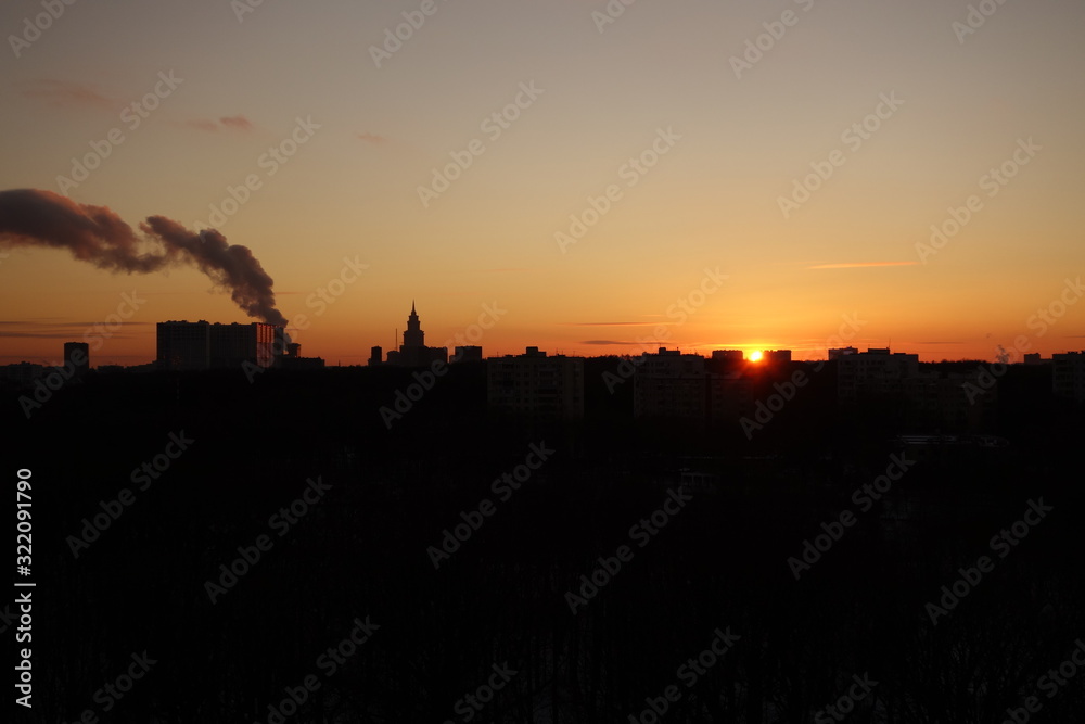 Sunset with a plume of smoke in black and orange in Moscow in winter