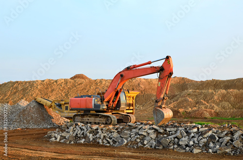 Heavy tracked excavator load stone, old asphalt or concrete waste into a mobile jaw crusher machine. Crushing and processing into gravel for recycling in concrete or cement production. photo