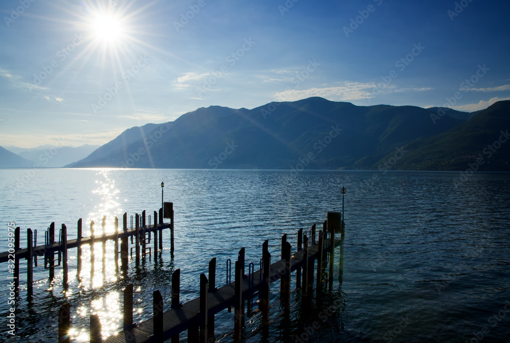 Pier with Sunbeam and Mountain on Alpine Lake Maggiore in Ticino, Switzerland.