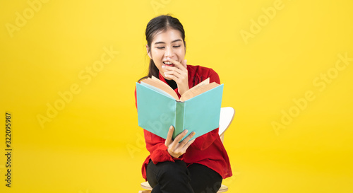 Asian women are reading a book or novel, enjoying and happy, the woman is opening a book in the hand and accidentally read it on yellow background with copy space.