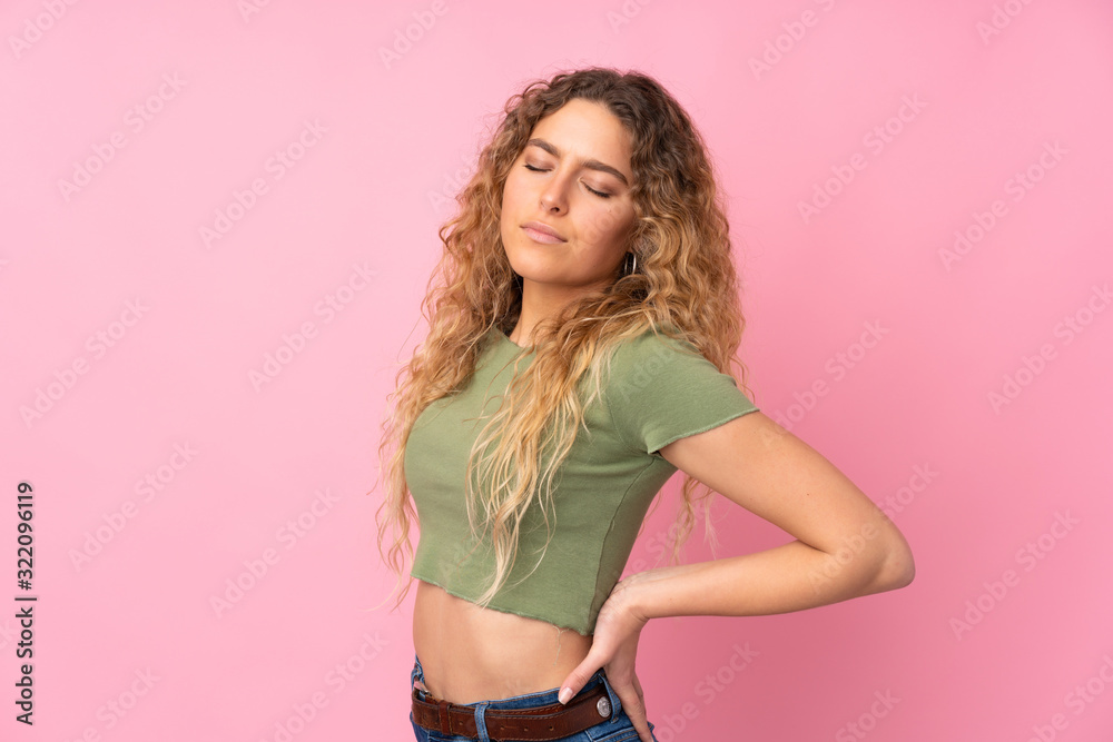 Young blonde woman with curly hair isolated on pink background suffering from backache for having made an effort Young blonde woman with curly hair isolated on pink background suffering from backache for having made an effort